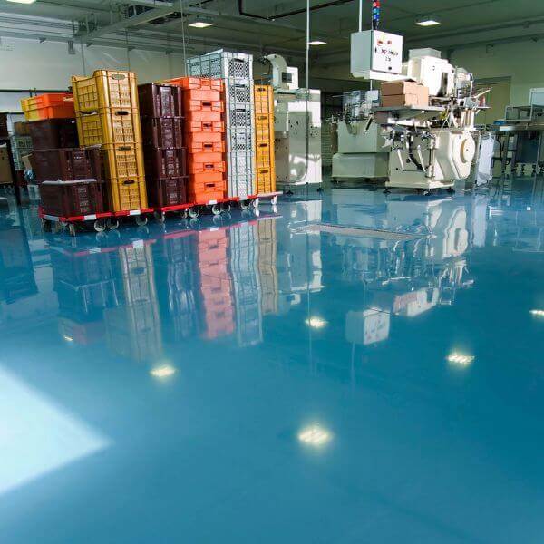 Clean blue epoxy flooring in an industrial area with stacked crates and equipment, installed by Epoxy Flooring Guys Perth.